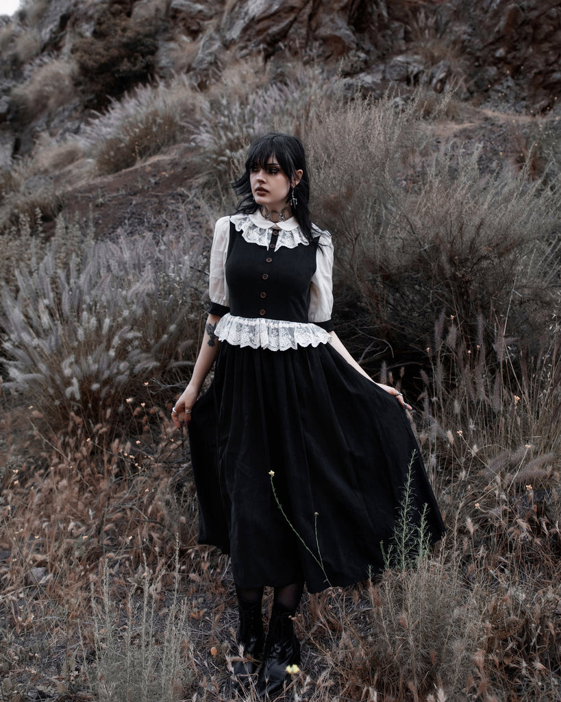 Woman in a black and white dress standing in a desert landscape with rocky mountains in the background.
